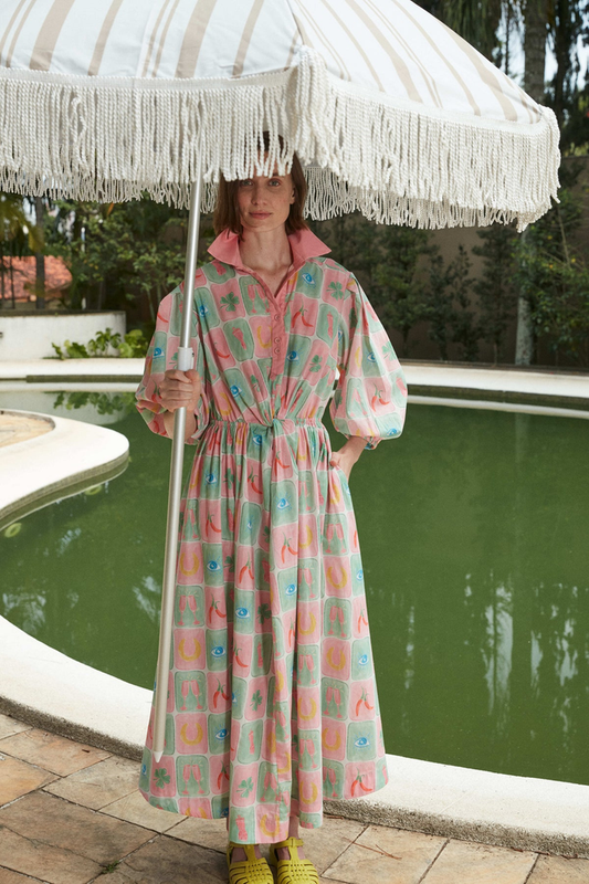 Woman wearing a colorful Talismã Collection dress by Hanna Inaiáh holding a fringed umbrella near a pool