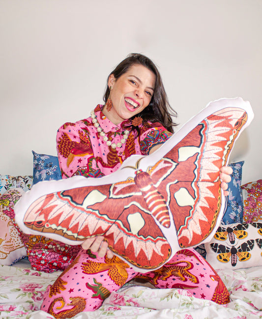Woman wearing vibrant pink patterned outfit holding a large butterfly-shaped pillow celebrating Women’s Month collection